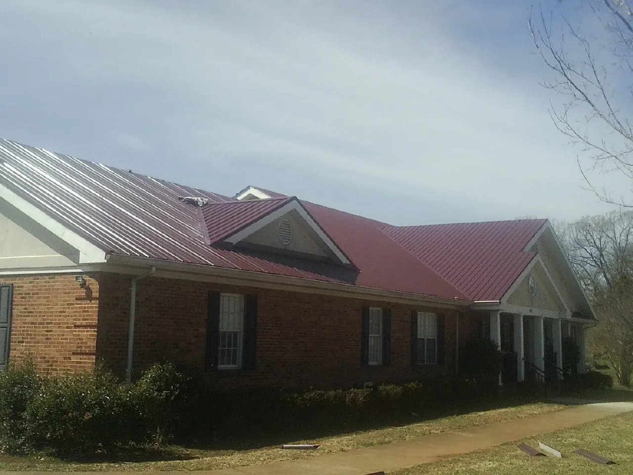 Red metal roof with gabled entries on a long brick building, from a Hail Damage Roof Repair job in Verplanck