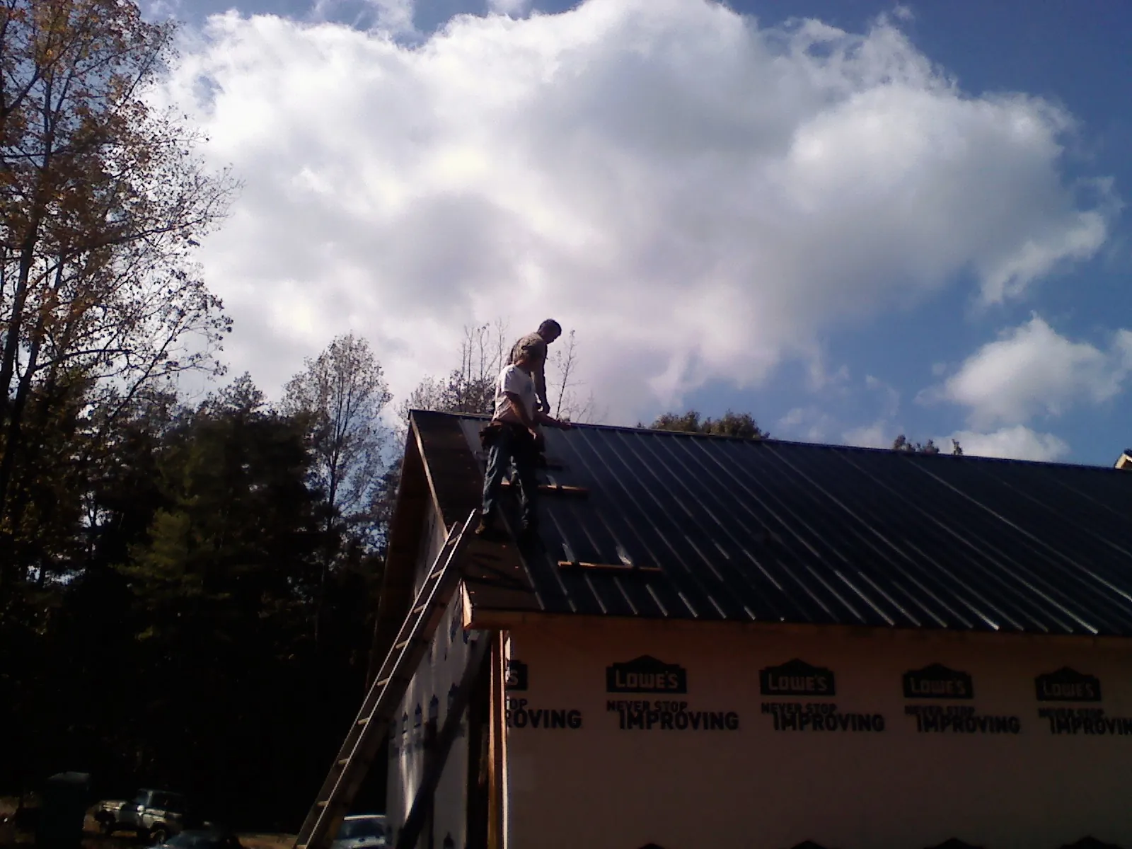 Roofer fastening dark metal panels high against a cloudy sky, from a Roof Inspection job in Verplanck