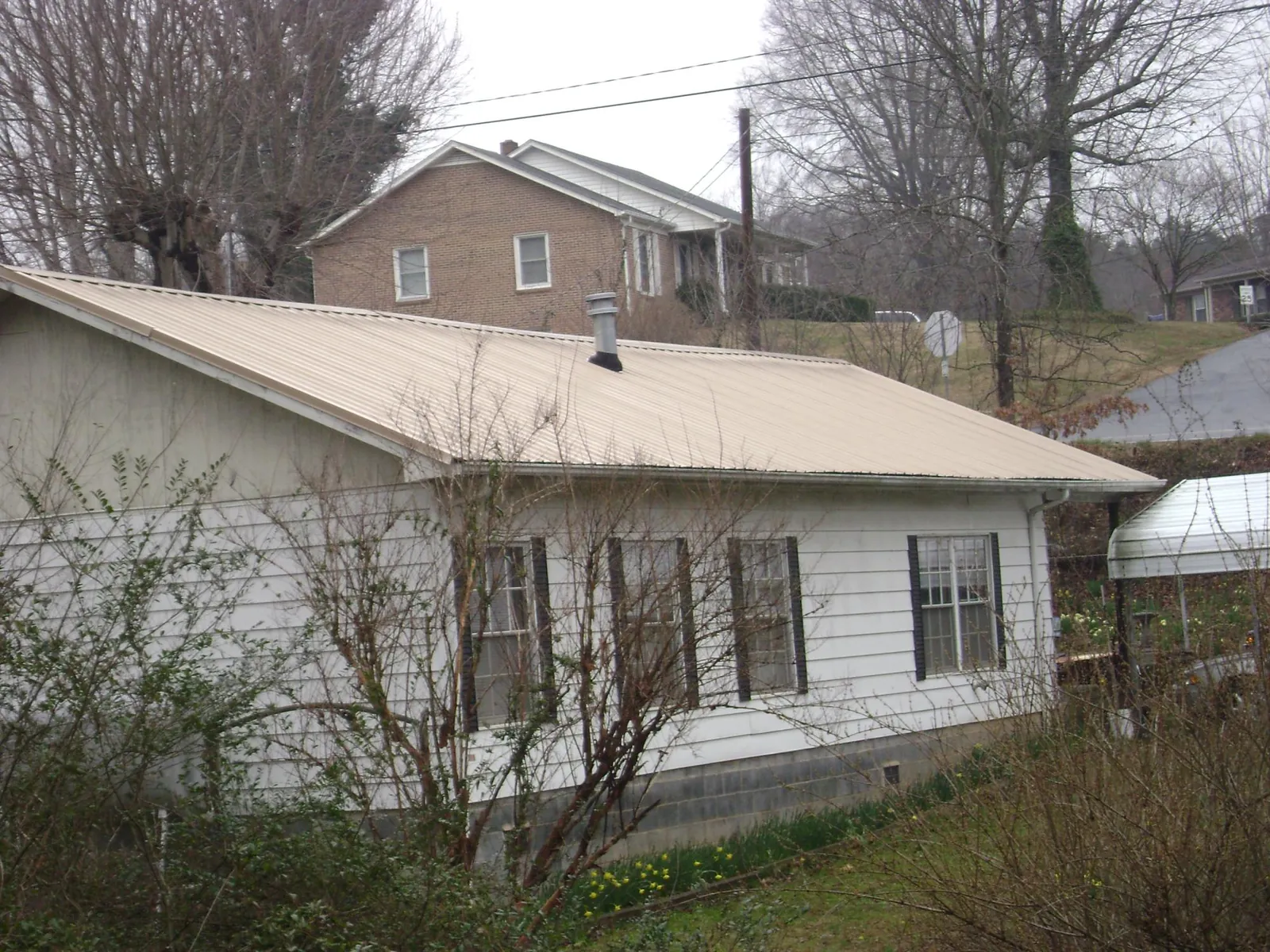 Tan metal roof on a white sided house set into a hillside — Commercial Roofing by Roofing Brothers in Verplanck